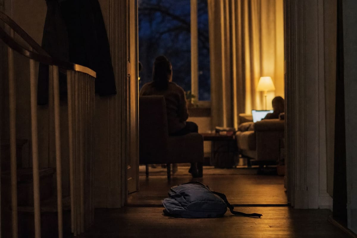 A school bag dropped on a hallway floor, warm light coming from a room beyond
